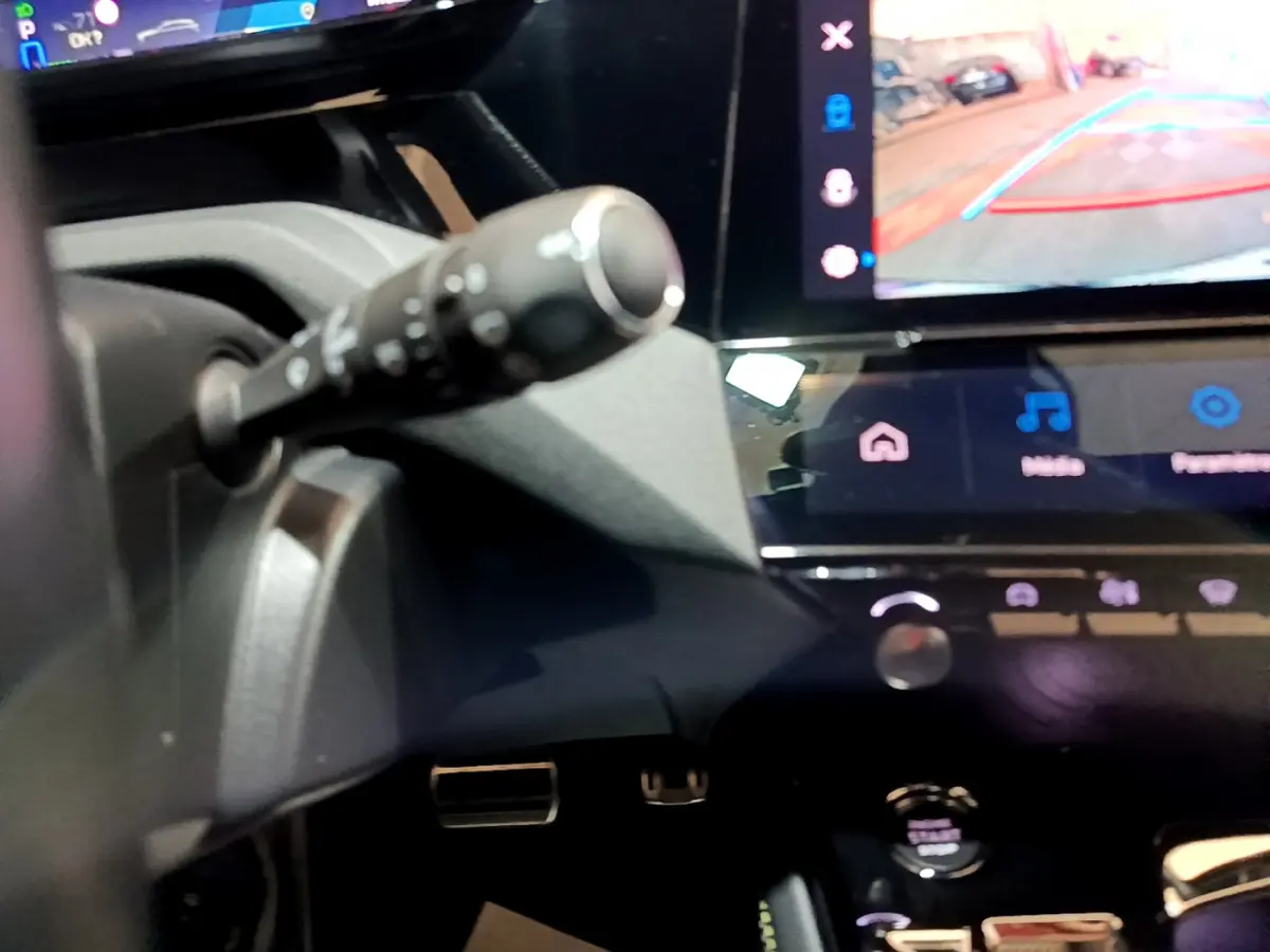 Gros plan sur la commande de clignotant et l'écran tactile affichant la caméra de recul dans l'habitacle noir d'une Peugeot 308 PHEV blanche.