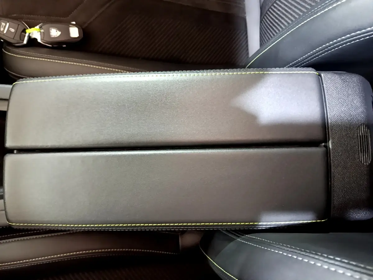 Vue rapprochée de l'accoudoir central noir avec surpiqûres vertes dans l'habitacle de la Peugeot 308 PHEV 180 GT blanche.