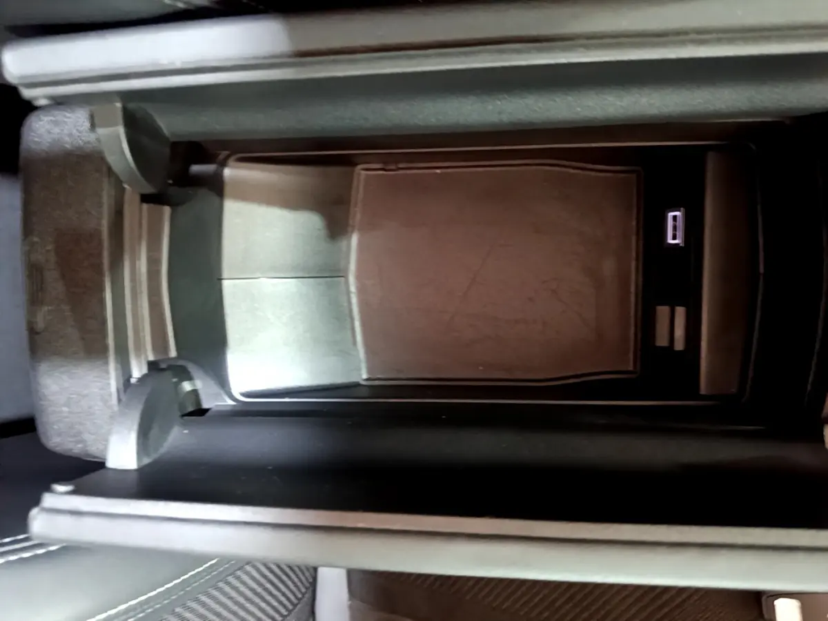 Vue rapprochée de la console centrale noire avec compartiment de rangement et port USB dans une Peugeot 308 PHEV 180 GT blanche.