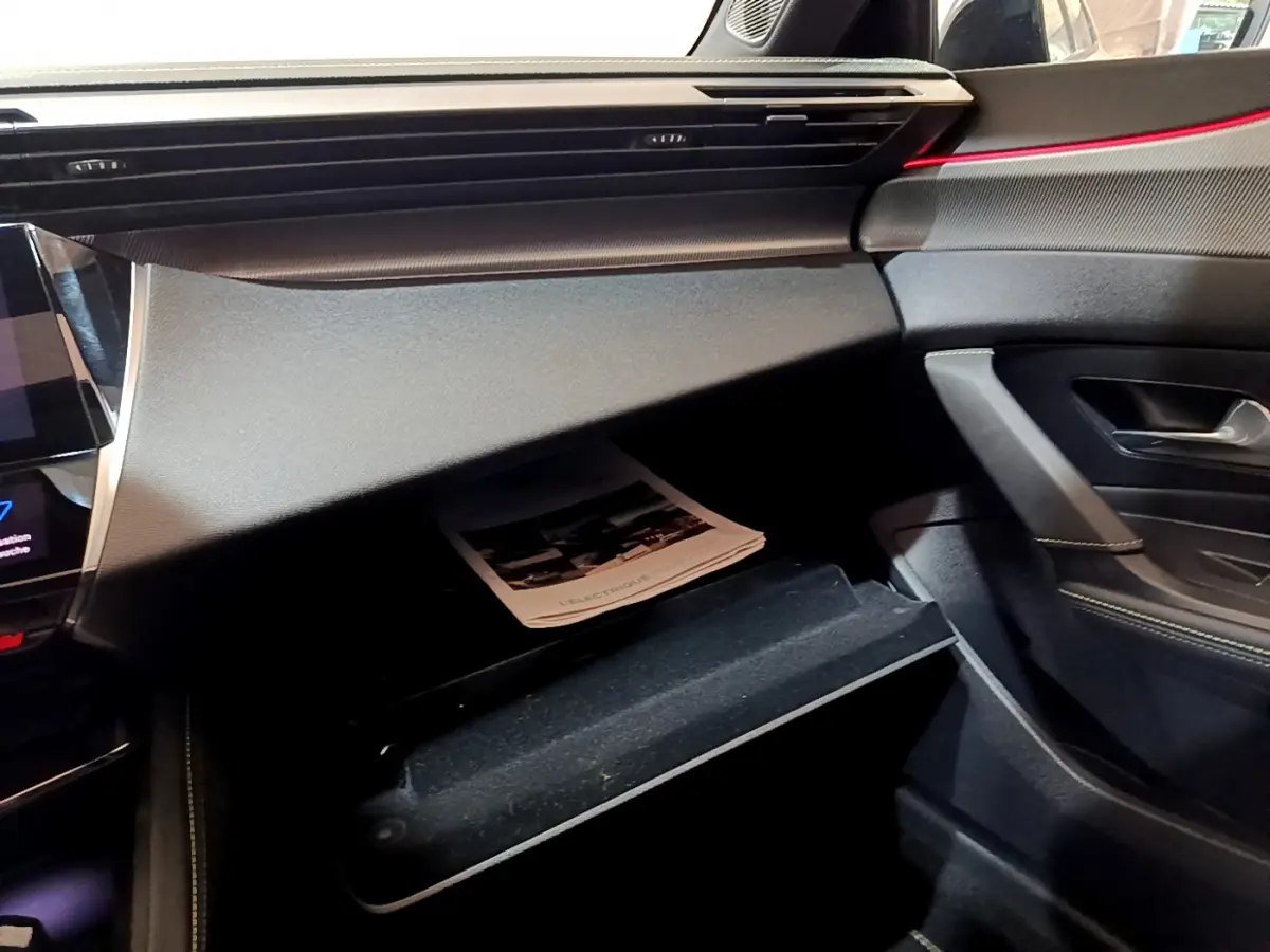 Intérieur côté passager de la Peugeot 308 PHEV 180 E-EAT8 GT 2022, tableau de bord noir avec boîte à gants ouverte.
