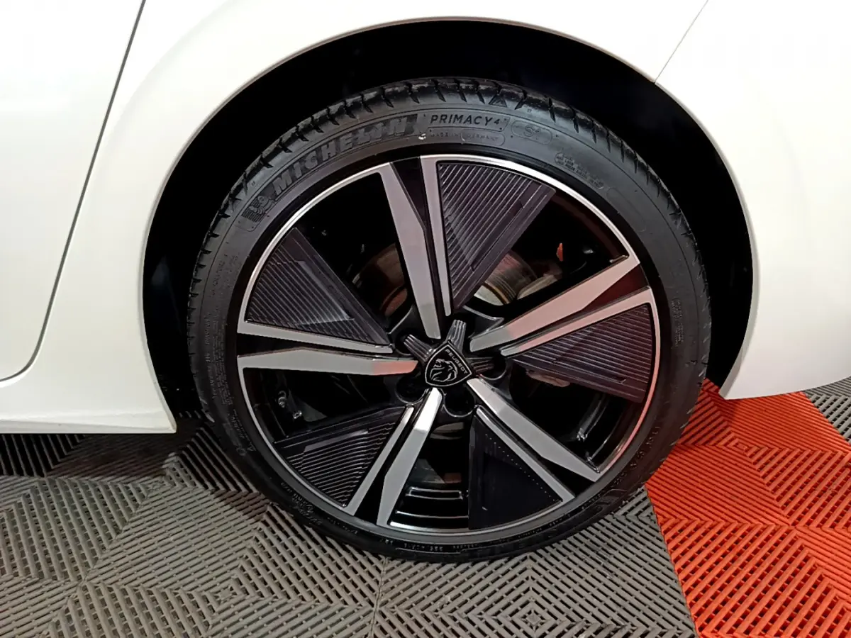 Gros plan sur la roue avant droite noire et argentée du Peugeot 308 PHEV blanc, soulignant la jante au design moderne.