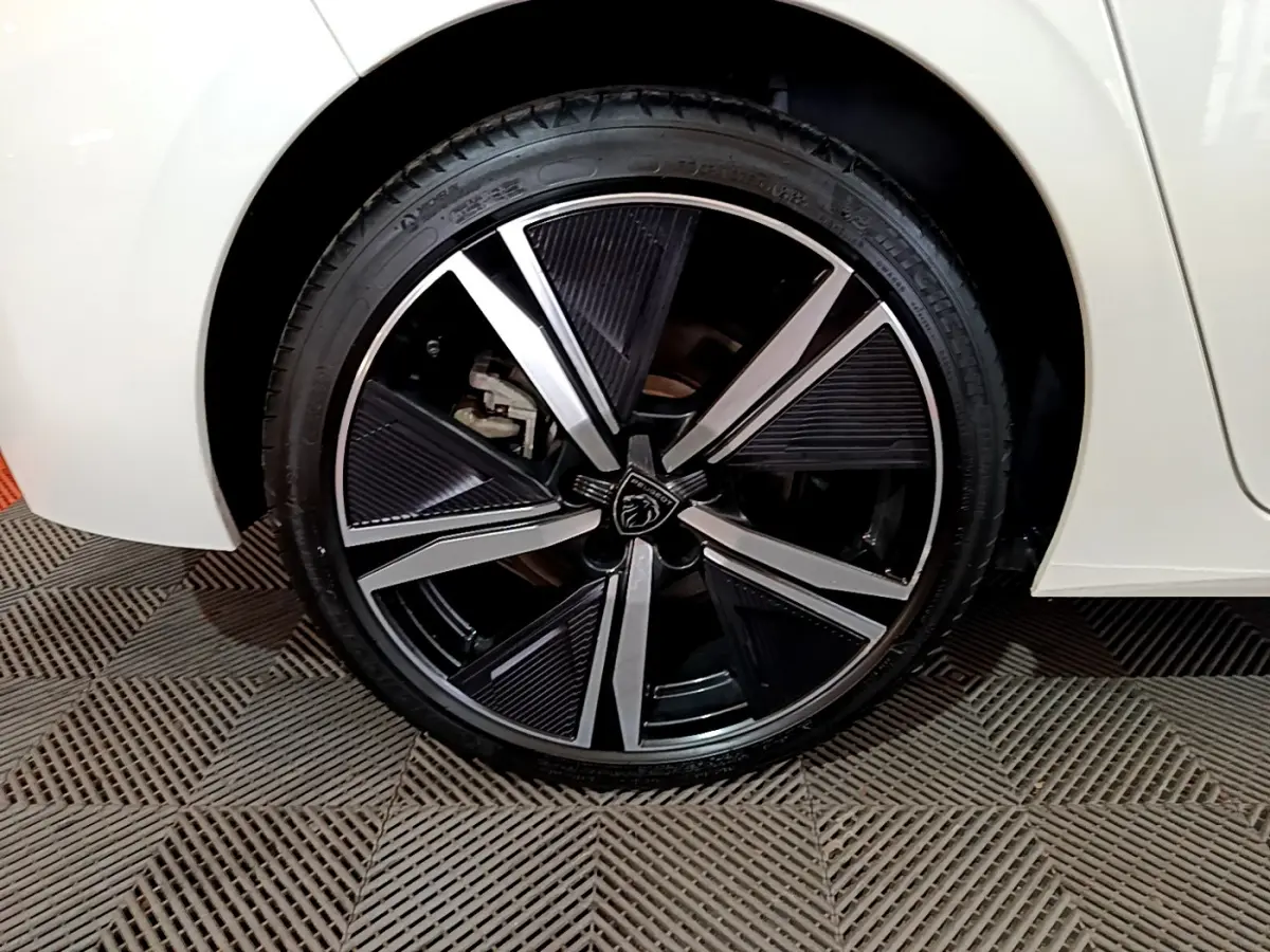Gros plan sur la roue avant droite d'une Peugeot 308 PHEV 180 E-EAT8 GT blanche avec jante alliage noire et argentée.