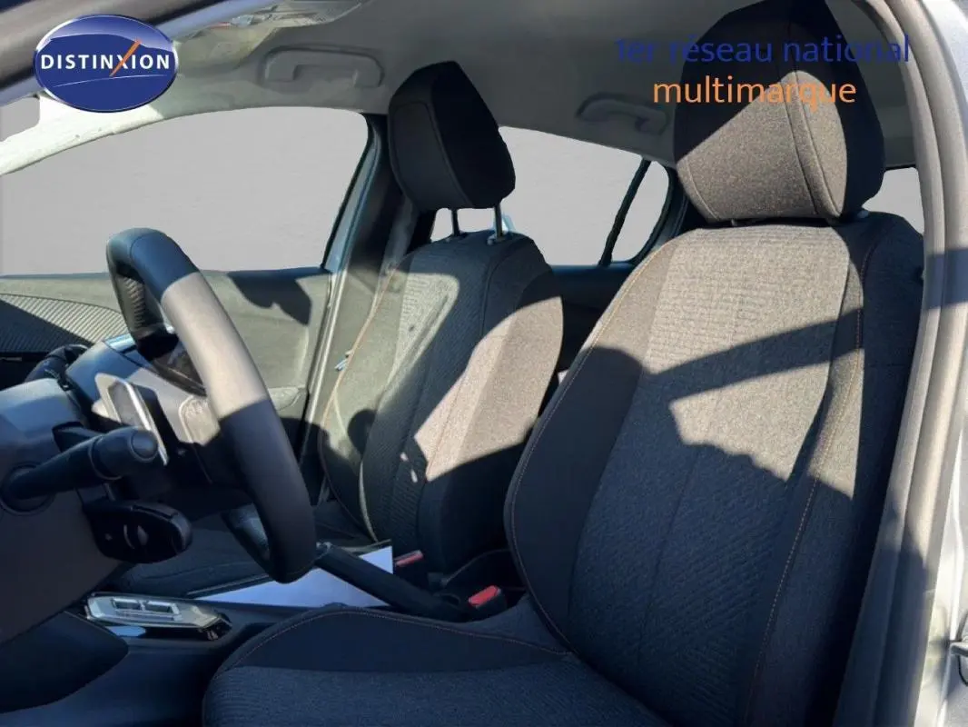 Vue intérieure côté conducteur de la Peugeot 208 gris 2025, mettant en valeur les sièges en tissu et le volant cuir.