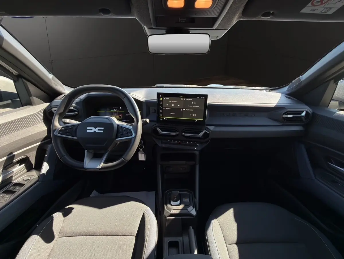 Vue intérieure avant du Dacia Duster gris foncé 2025, volant cuir multifonctions et écran tactile central visible.