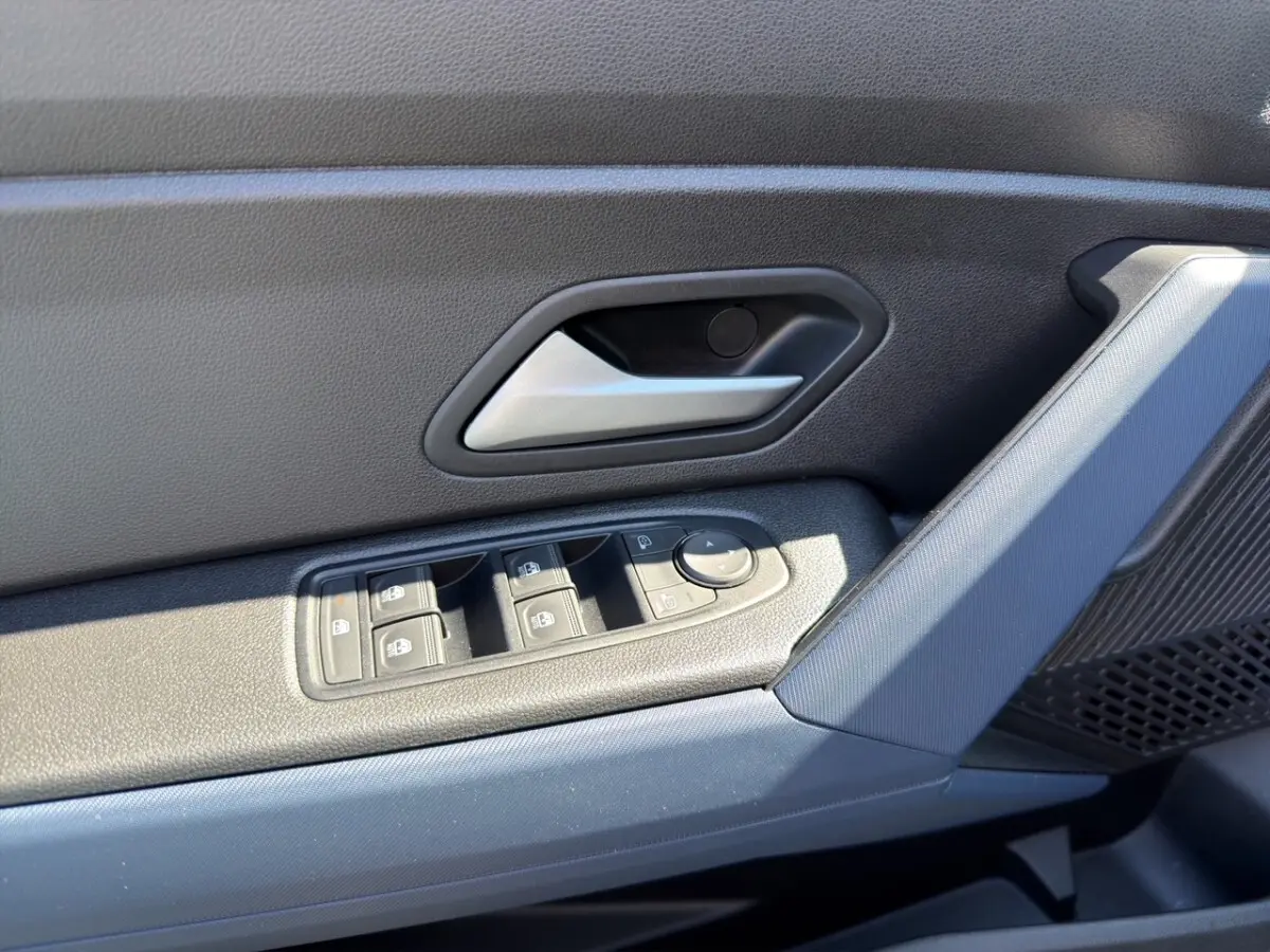 Gros plan sur la porte côté conducteur du Dacia Duster gris foncé, montrant les commandes des vitres et la poignée intérieure.