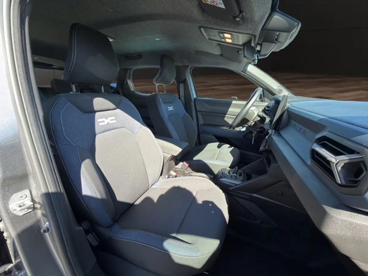Vue intérieure côté conducteur du Dacia Duster gris foncé 2025, sièges tissu avec logo DC et tableau de bord moderne.