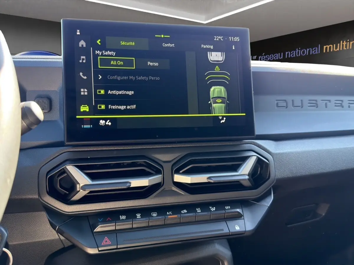 Vue intérieure du tableau de bord du Dacia Duster gris foncé, avec écran tactile central affichant les aides à la conduite.