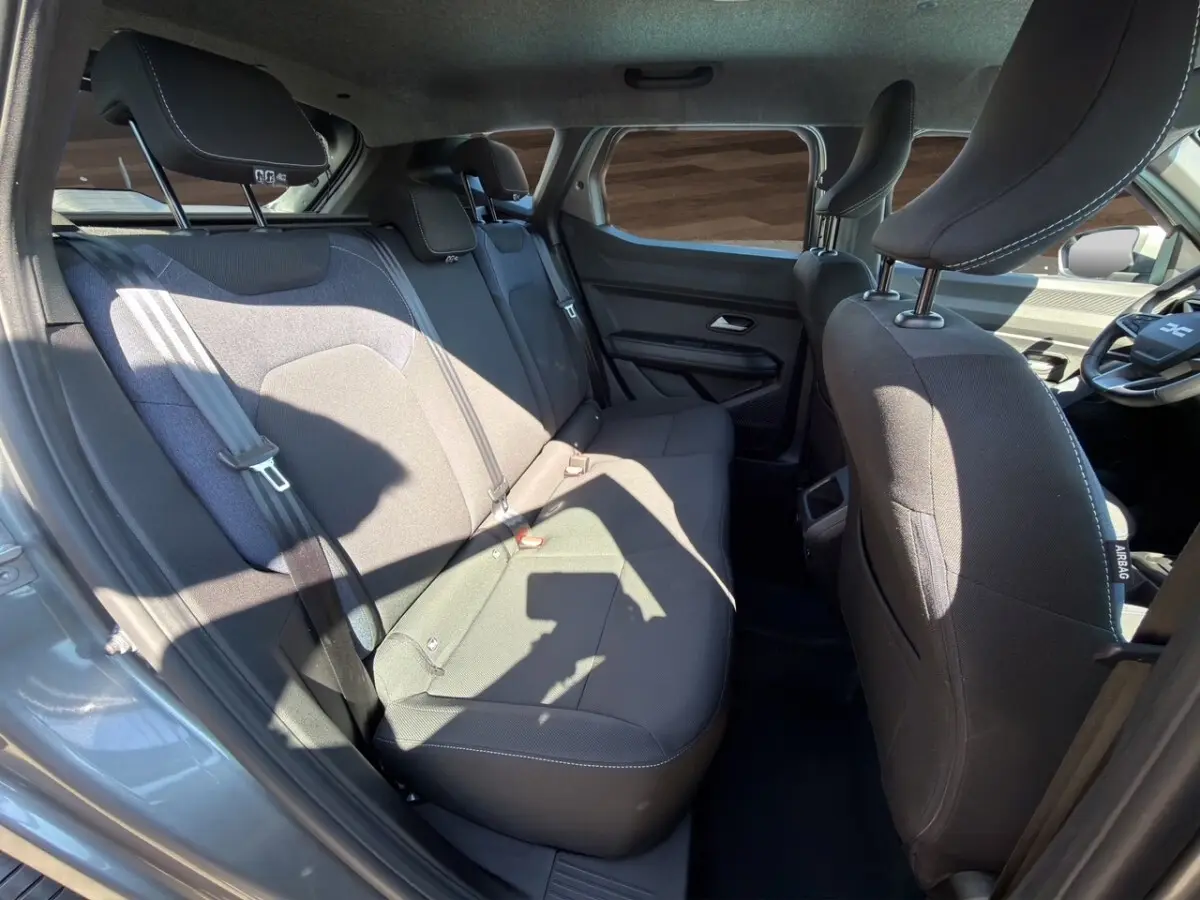 Vue intérieure arrière côté droit du Dacia Duster gris foncé 2025, montrant la banquette 3 places et les sièges avant.