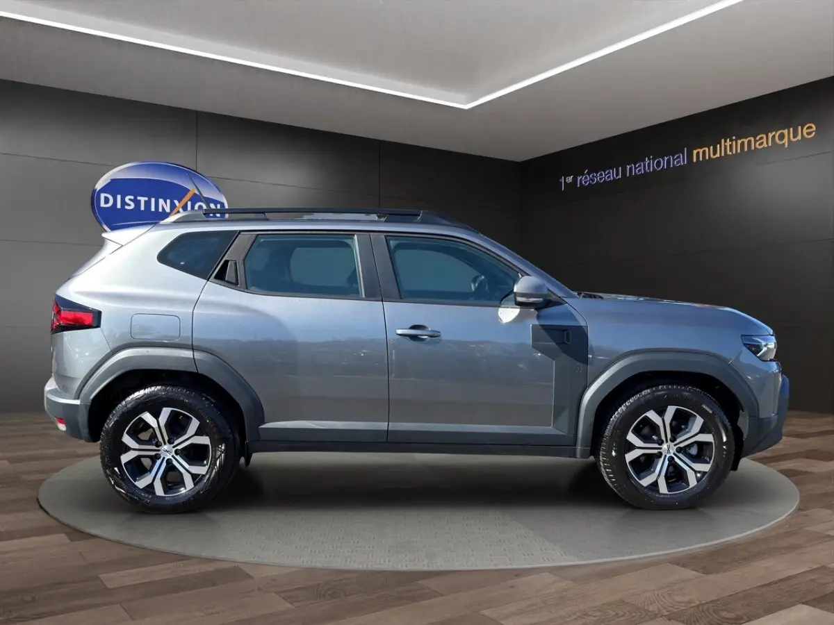 Vue de profil côté gauche d'un Dacia Duster gris foncé 2025 avec rails de toit noirs et jantes alliage.