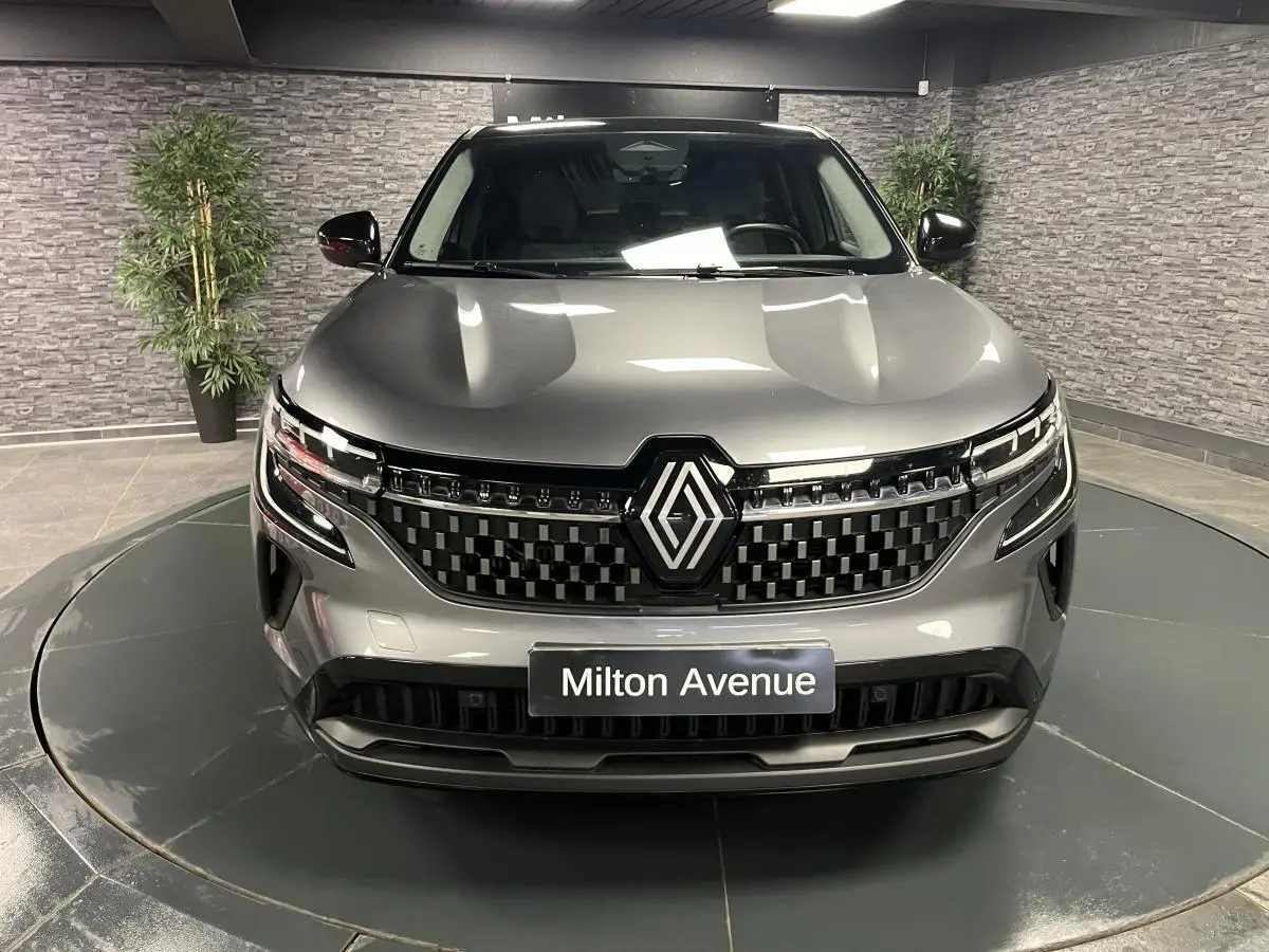 Vue avant d'un Renault Austral gris avec calandre à damier chrome sombre et toit noir étoilé en intérieur showroom.