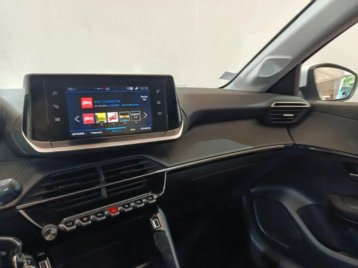 Vue intérieure côté passager du tableau de bord noir et écran tactile 7 pouces de la Peugeot 208 blanche PureTech 2020