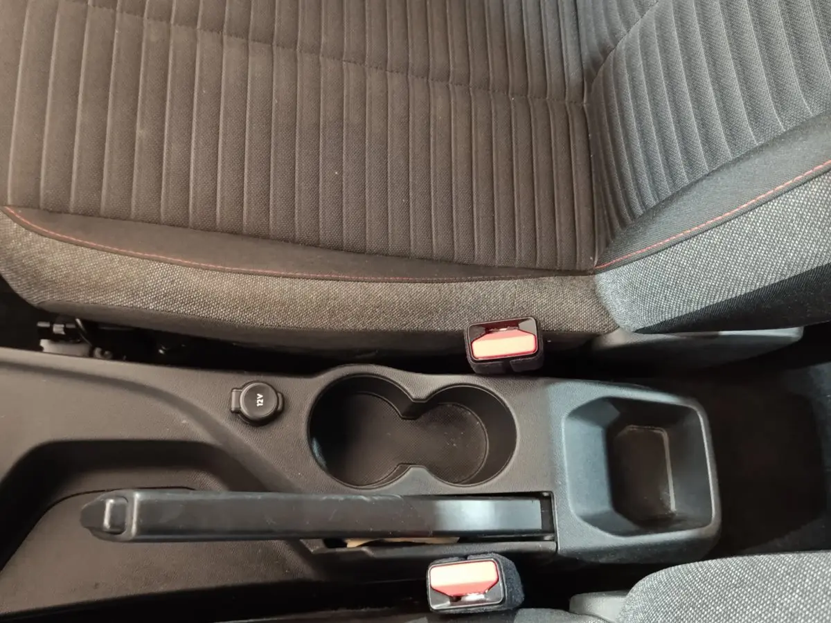 Vue plongeante sur la console centrale noire et les sièges tissu gris foncé avec surpiqûres rouges d'une Peugeot 208 blanche.