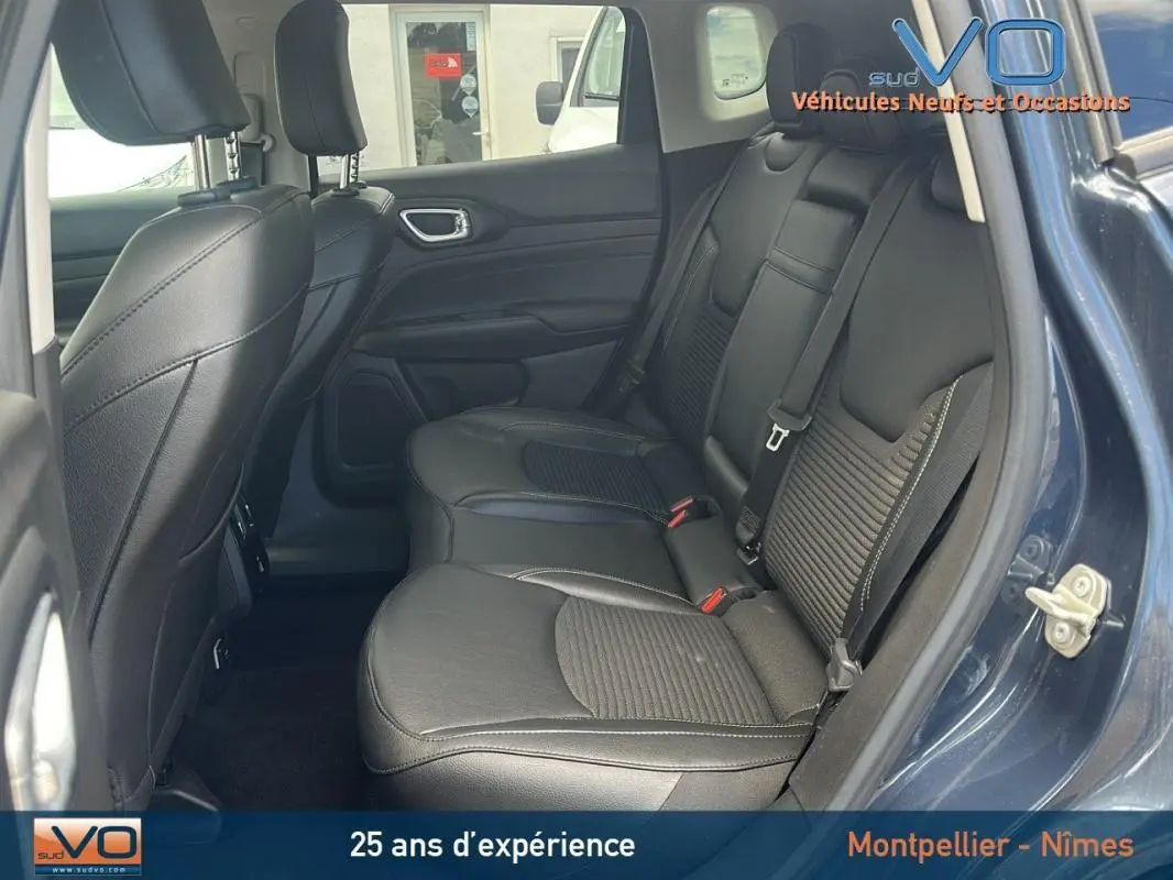 Vue intérieure arrière du Jeep Compass bleu 2023, sièges en cuir noir avec accoudoir central et ceintures visibles.