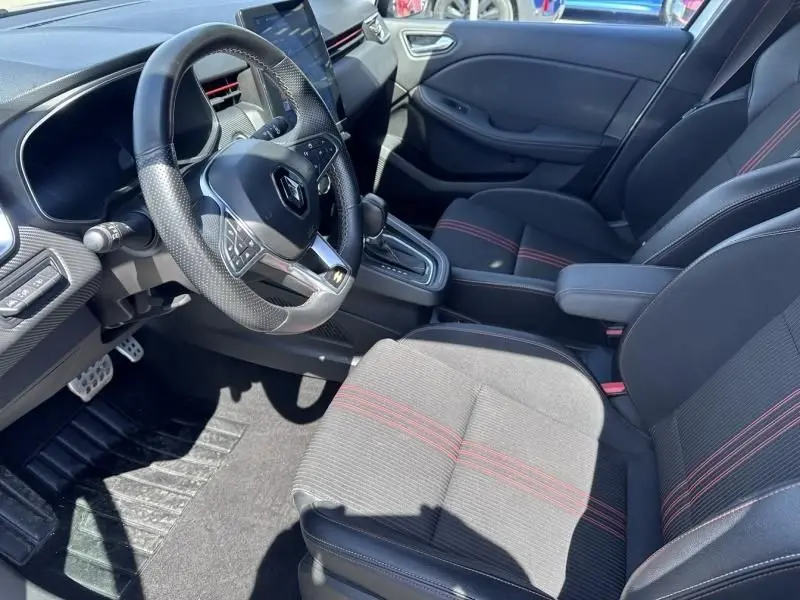 Intérieur de Renault Clio V 1.6 E-Tech hybride 2022, vue côté conducteur, sièges noirs avec surpiqûres rouges et volant multifonction.
