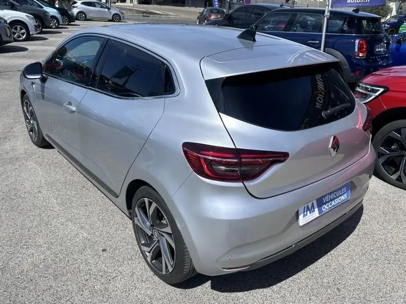 Renault Clio V gris métal vue 3/4 arrière droit, finition RS Line avec jantes alliage et vitres teintées.