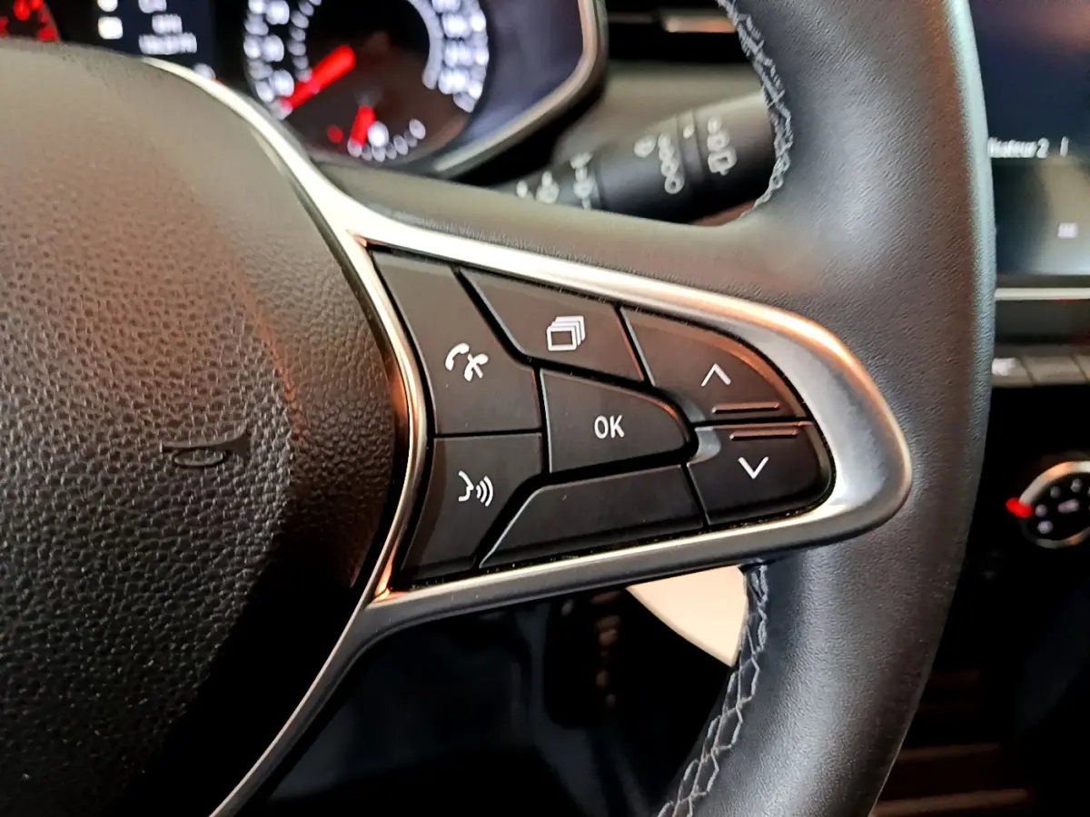 Gros plan sur les commandes multifonctions du volant cuir noir de la Renault Clio Business blanche de 2021.