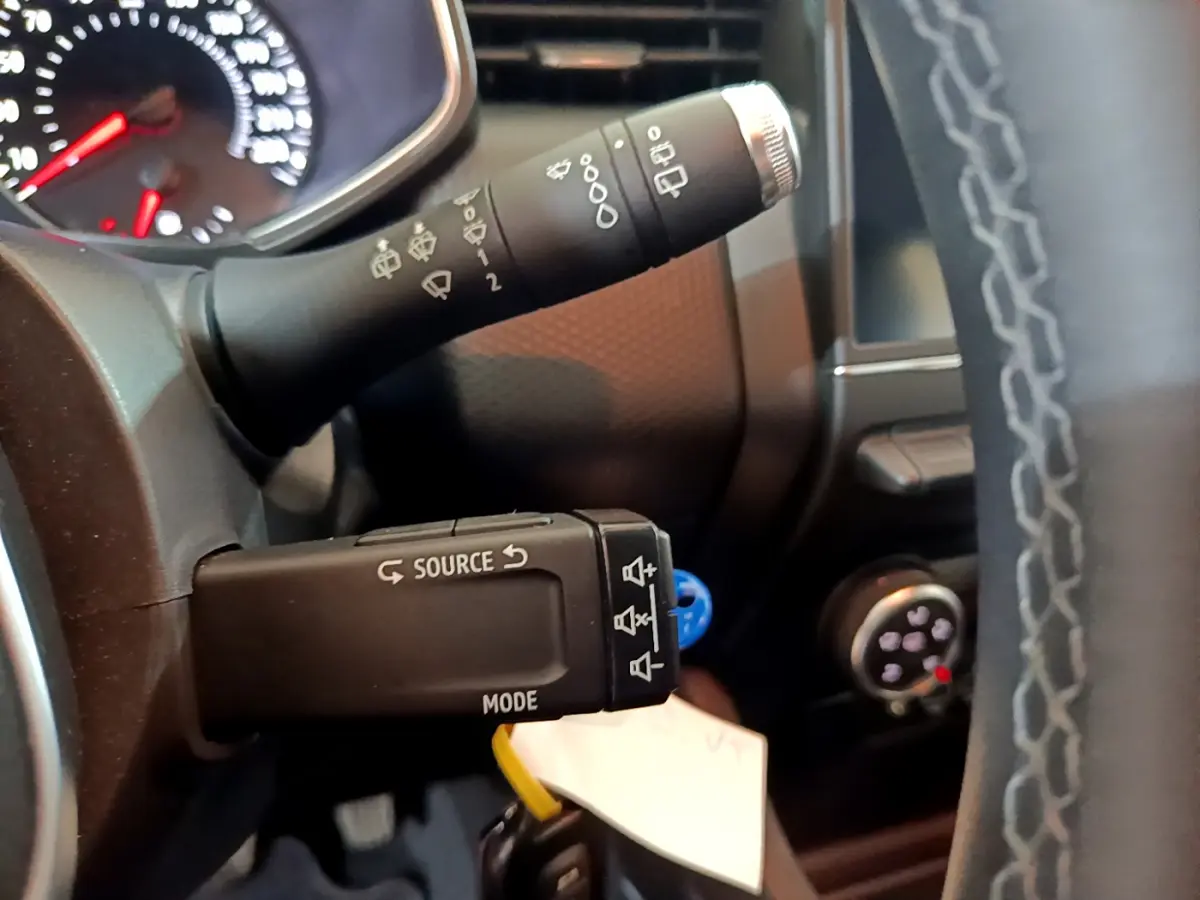 Gros plan sur la commande multifonction noire à gauche du volant cuir d'une Renault Clio Business blanche, tableau de bord en arrière-plan.