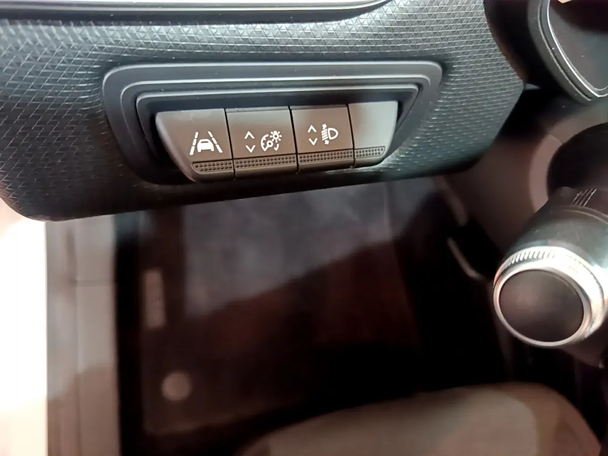 Gros plan sur les commandes d'assistance à la conduite sous le tableau de bord d'une Renault Clio Business blanche.