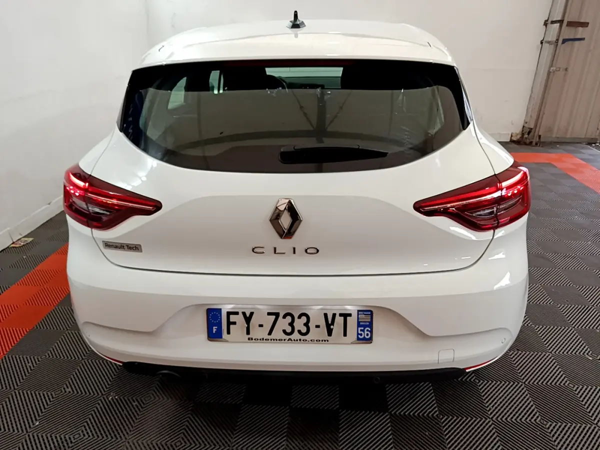 Vue arrière d'une Renault Clio blanche 2021 avec feux LED et logo Renault centré sur un sol à damier noir et orange.