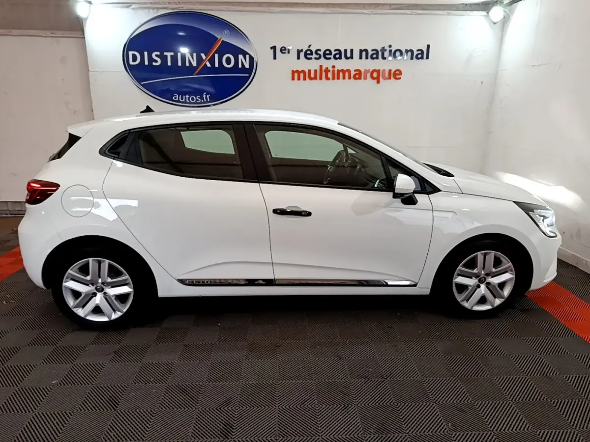Profil droit d'une Renault Clio Business blanche 2021, avec jantes alliage et poignées noires, en intérieur showroom.