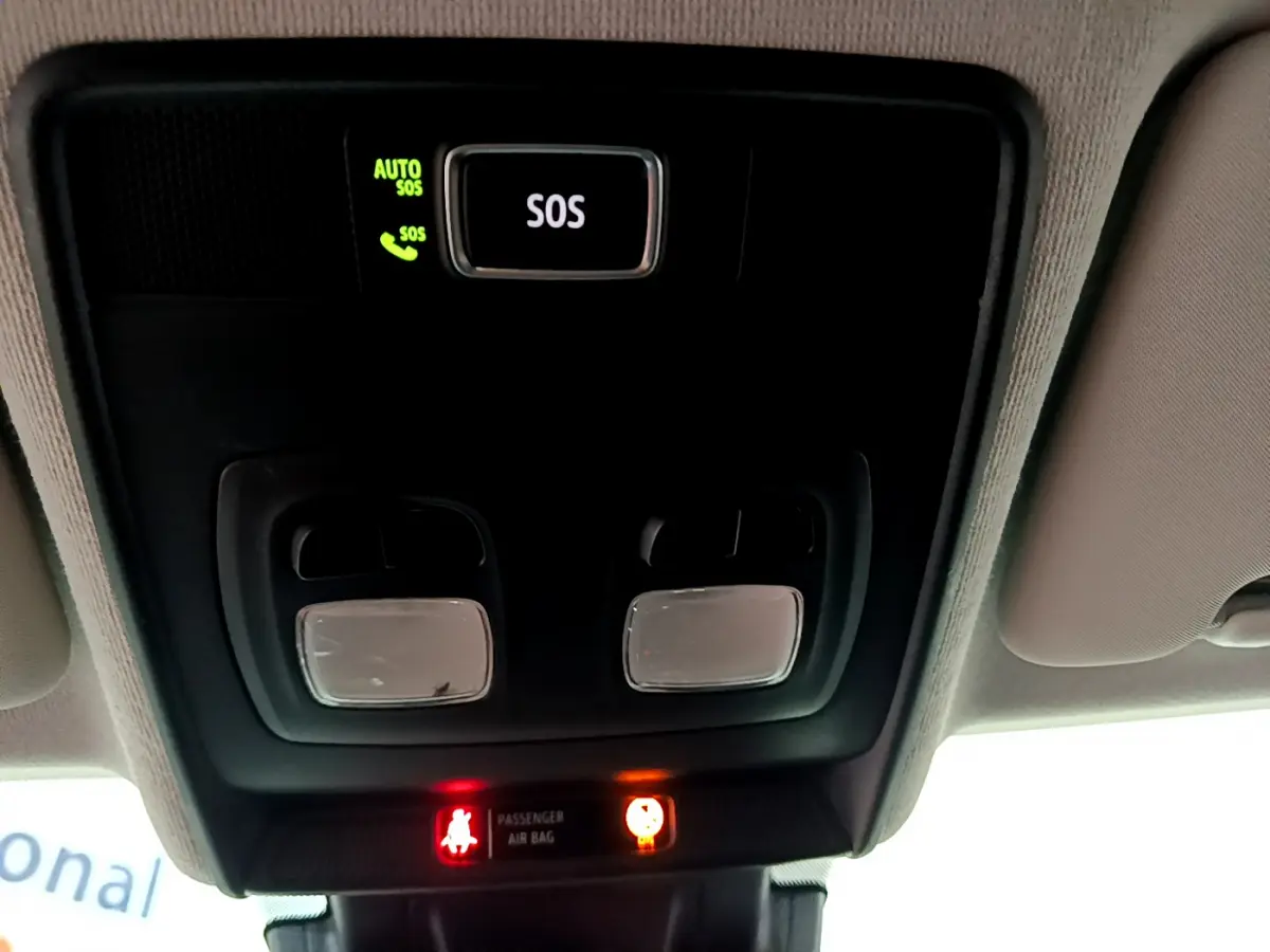 Vue en contre-plongée du plafonnier noir avec bouton SOS et voyants d'airbag allumés dans une Renault Clio blanche.