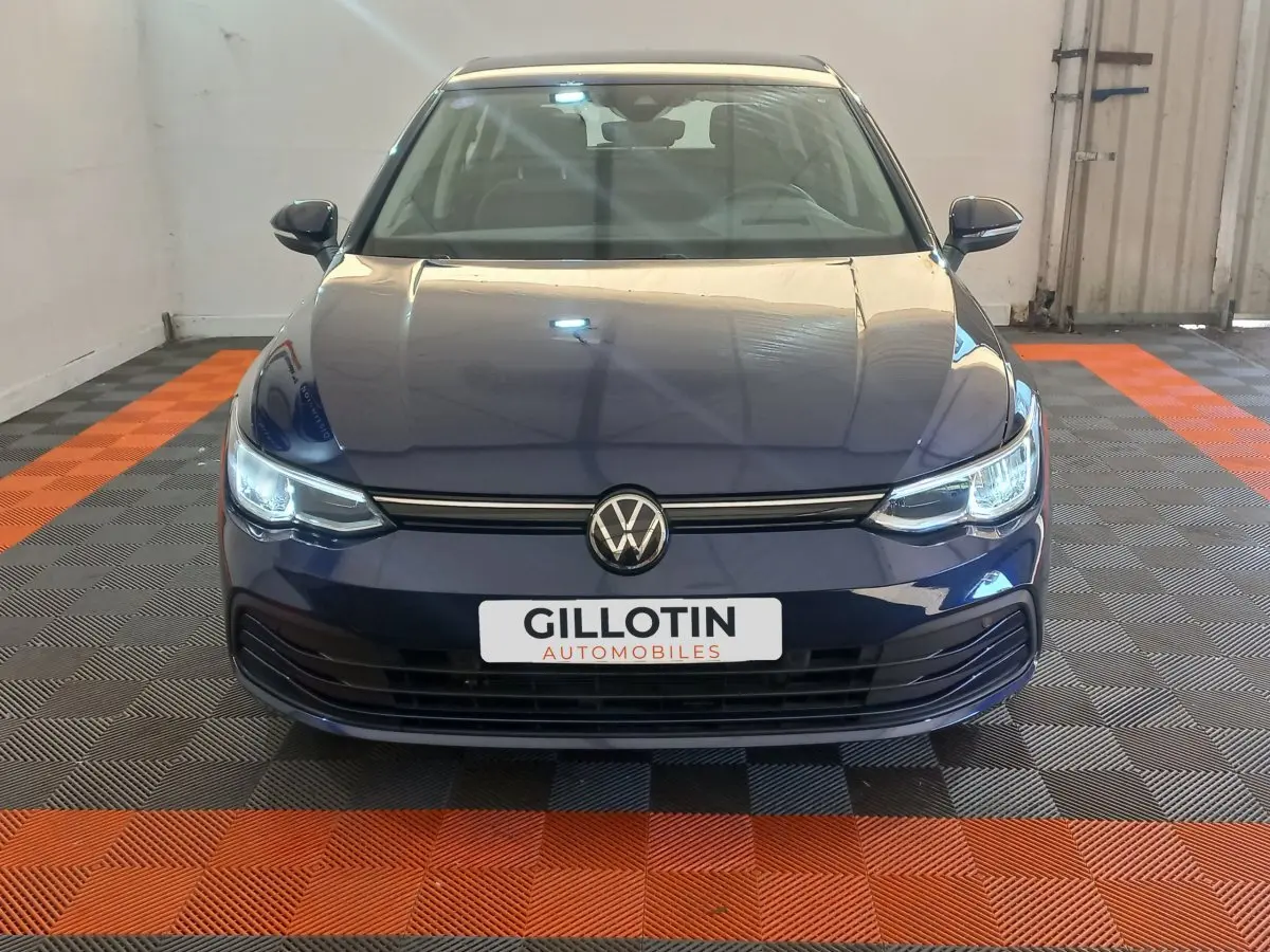 Volkswagen Golf bleu vue de face avec phares LED allumés et logo VW centré sur calandre noire.