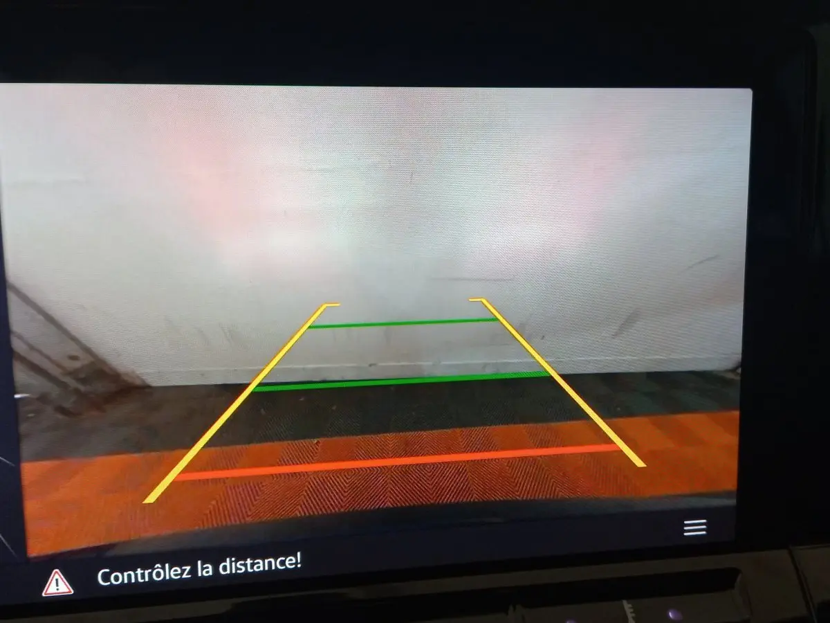 Affichage caméra de recul avec lignes de guidage colorées sur fond de mur blanc et sol carrelé, intérieur Volkswagen Golf 2022.