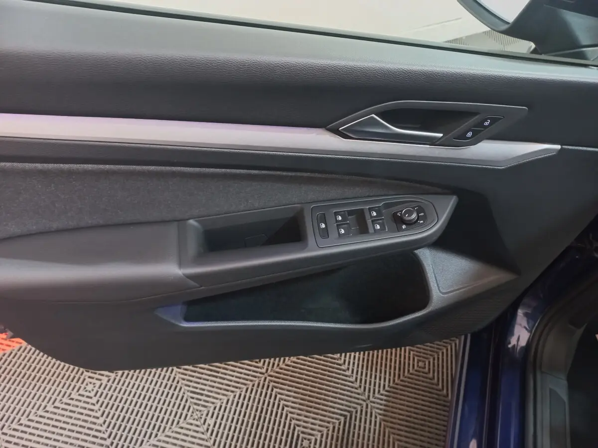 Vue rapprochée de la porte côté conducteur bleu de la Volkswagen Golf 1.5 ETSI avec commandes électriques et finition noire.