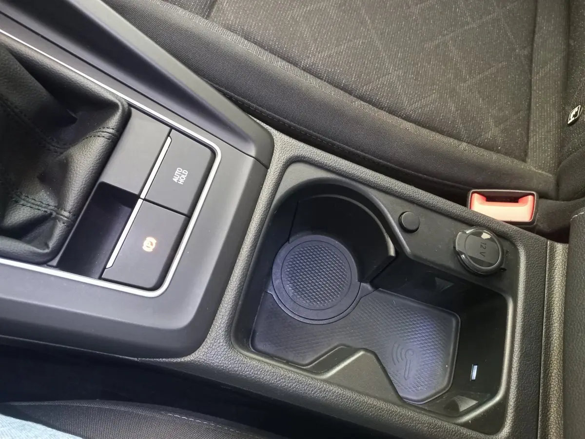 Gros plan sur la console centrale noire de la Volkswagen Golf 1.5 ETSI avec zone de recharge sans fil et prise 12V.