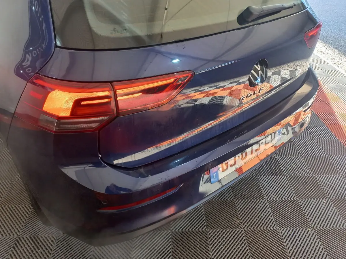Vue 3/4 arrière droite d'une Volkswagen Golf bleue 2022 avec feux arrière allumés et logo visible sur le coffre