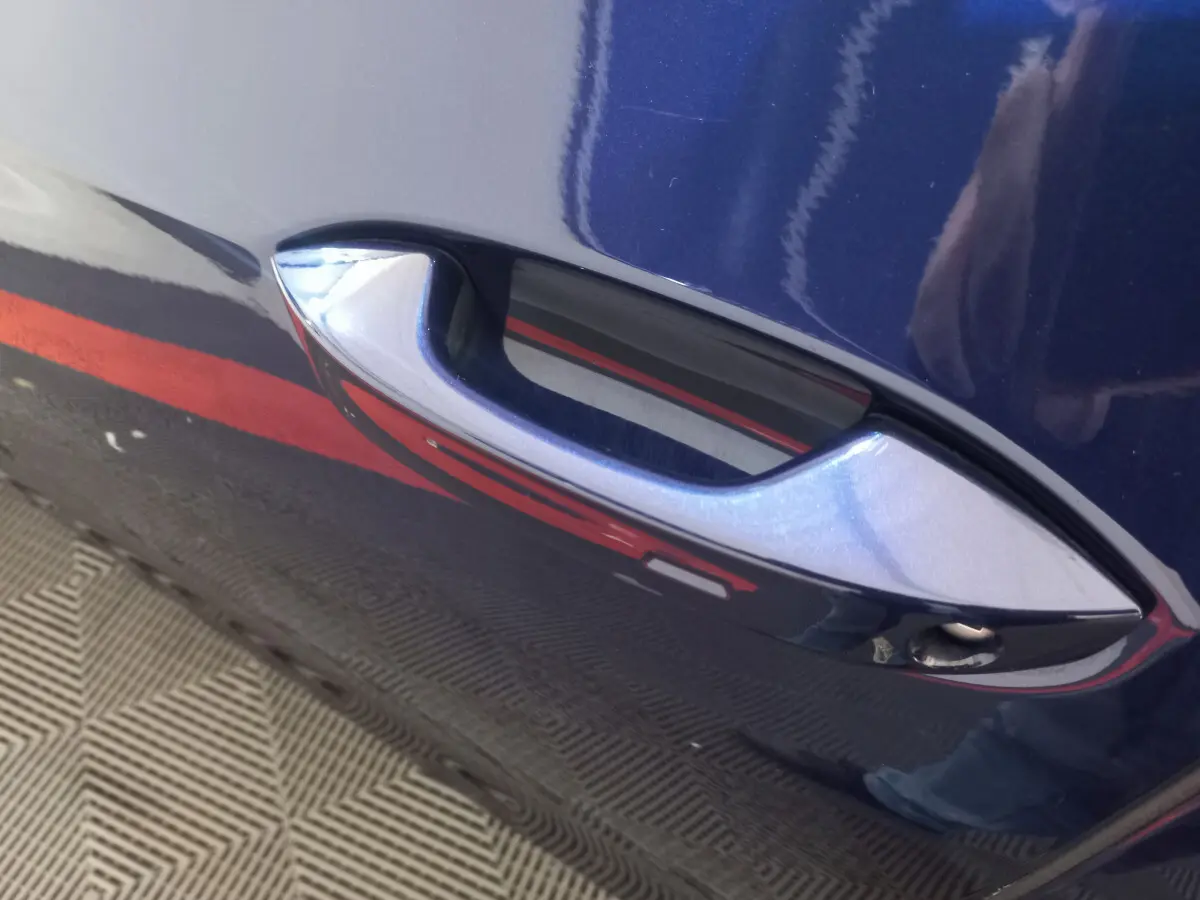 Poignée de porte avant droite bleu métallisé sur Volkswagen Golf 1.5 ETSI 2022, reflet rouge et sol texturé visible