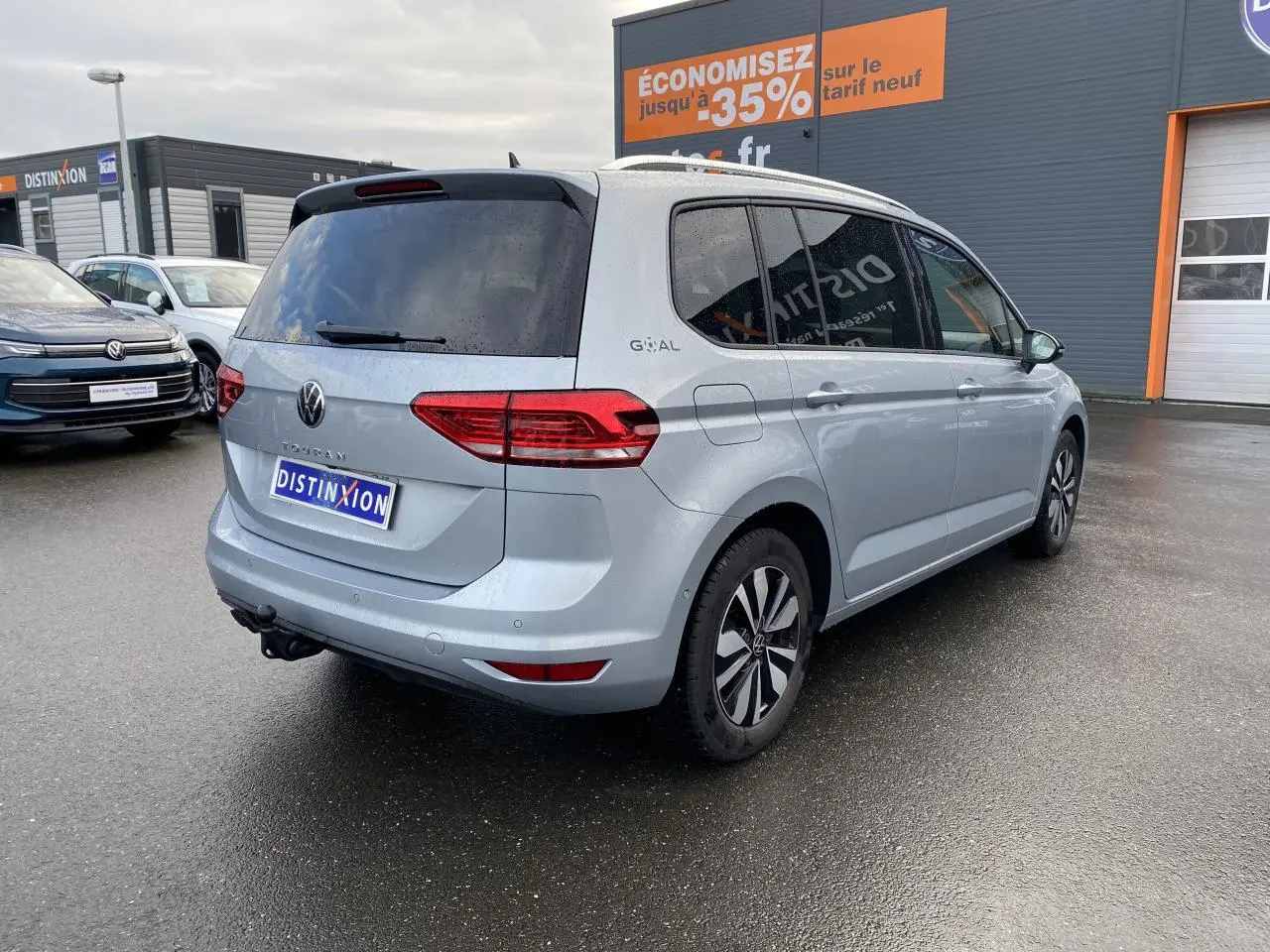 Vue 3/4 arrière droite d’un Volkswagen Touran 2025 gris argent métallisé avec attelage et vitres surteintées.