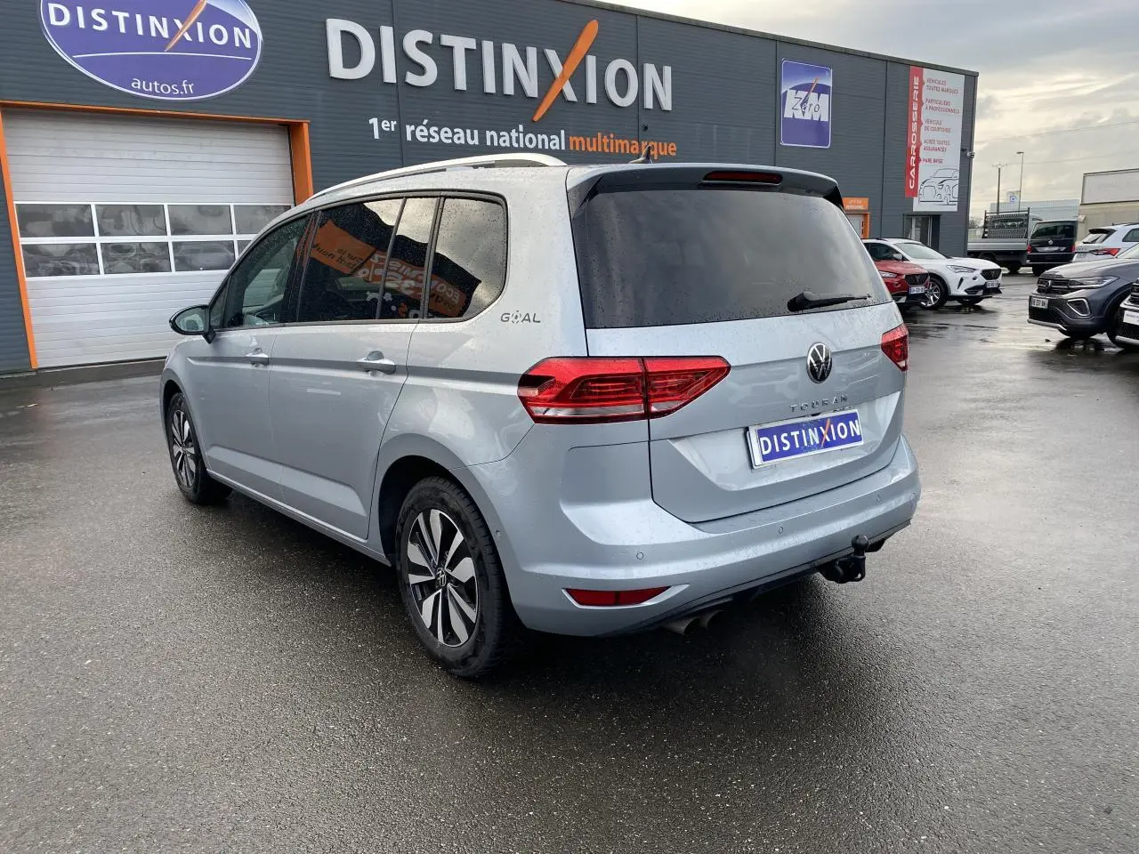 Volkswagen Touran 2025 gris Oyster, vue 3/4 arrière droit avec attelage escamotable et vitres arrière surteintées.