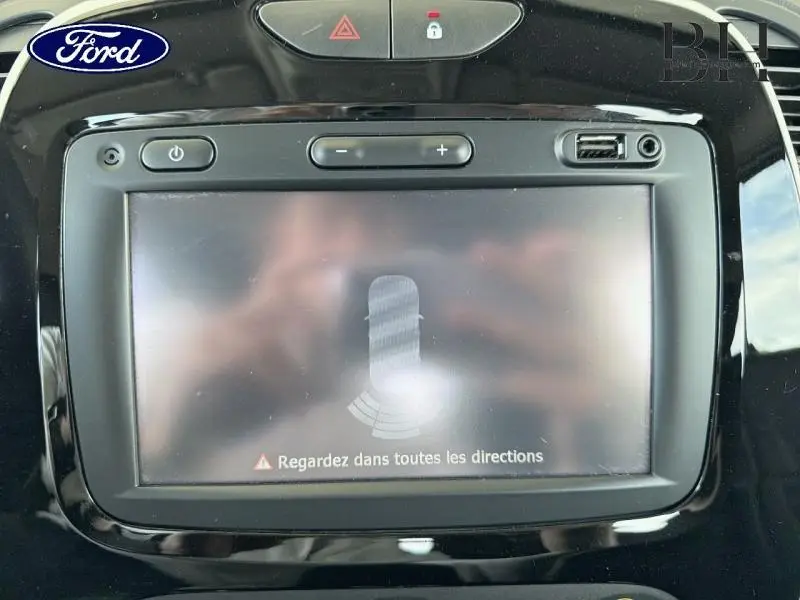 Écran tactile central du tableau de bord d’un Renault Captur gris platine, vue de face avec affichage d’alerte de proximité.