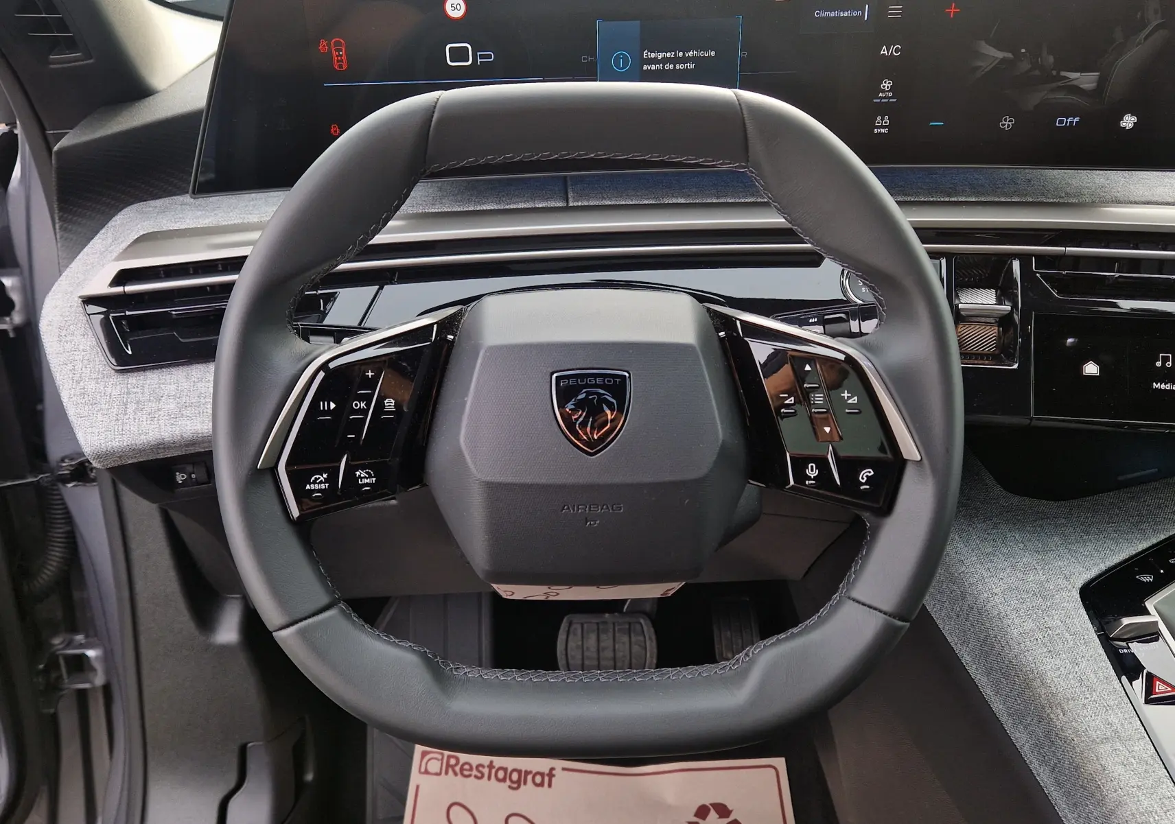 Vue intérieure centrée sur le volant cuir du Peugeot 3008 gris Artense 2025 avec écran panoramique 21 pouces en arrière-plan.