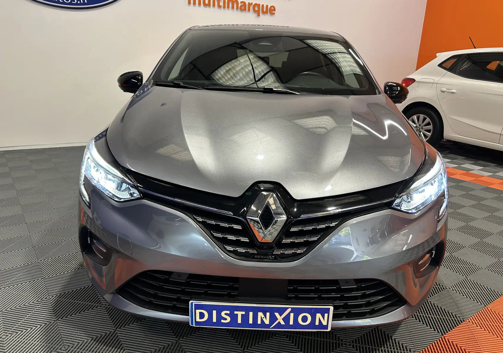 Vue avant d'une Renault Clio V TCe 90 TECHNO gris avec phares allumés et logo Renault bien visible.