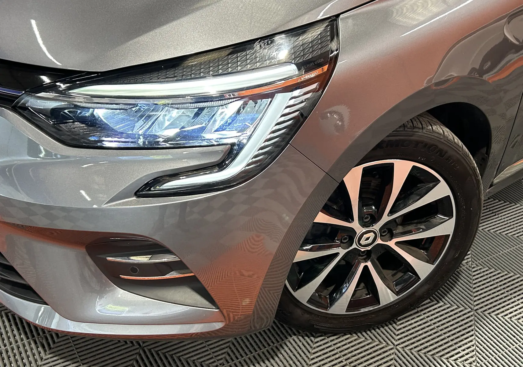 Gros plan sur l'avant droit gris métallisé de la Renault Clio V 2023, mettant en valeur son phare LED et sa jante alliage.
