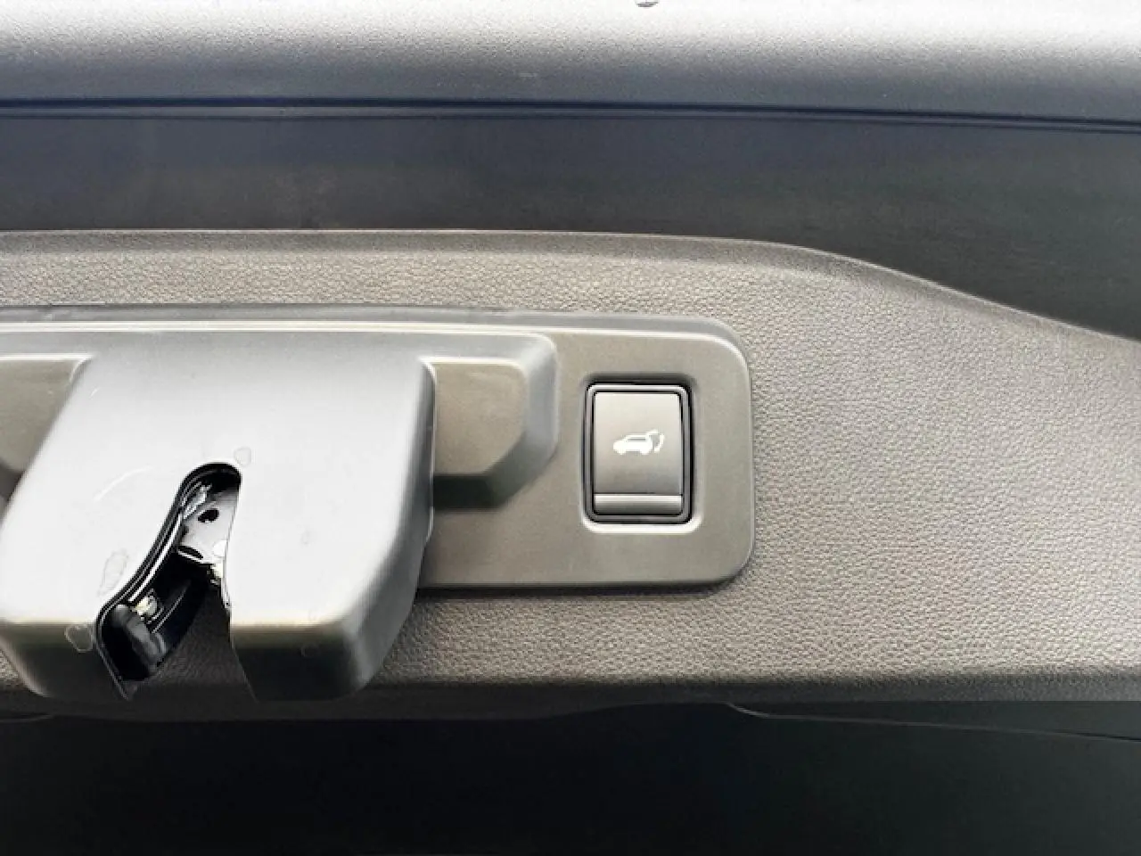 Gros plan sur le bouton d'ouverture du hayon du Renault Espace VI noir étoilé, situé sur le bord intérieur du coffre.