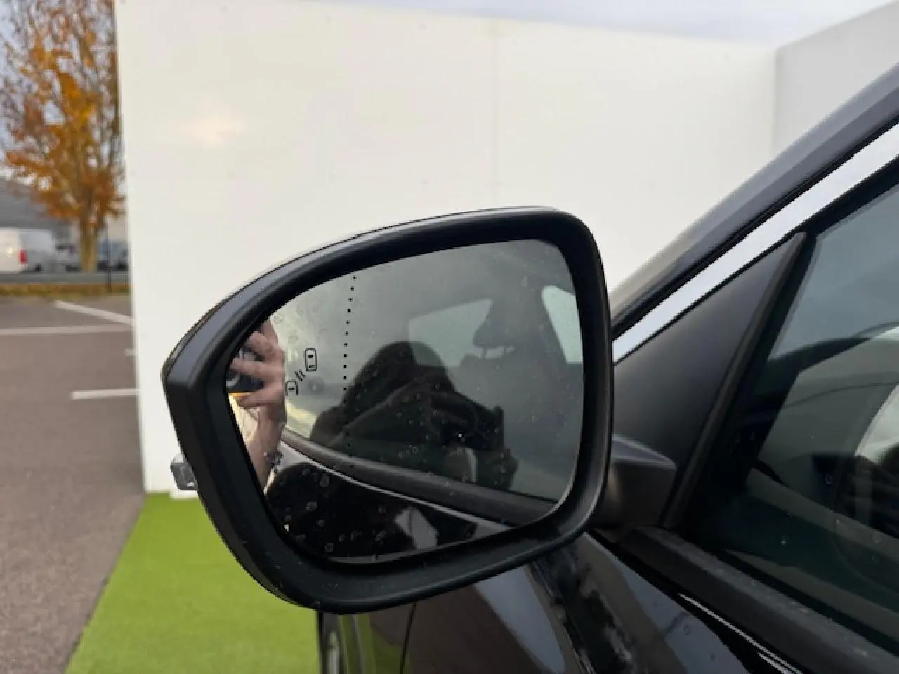 Rétroviseur extérieur côté gauche du Renault Espace VI noir étoilé, avec surface légèrement humide et reflet flou.