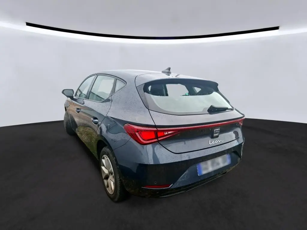 Vue 3/4 arrière droite d'une SEAT Leon gris métallisé 5 portes avec feux arrière reliés par une bande lumineuse rouge.