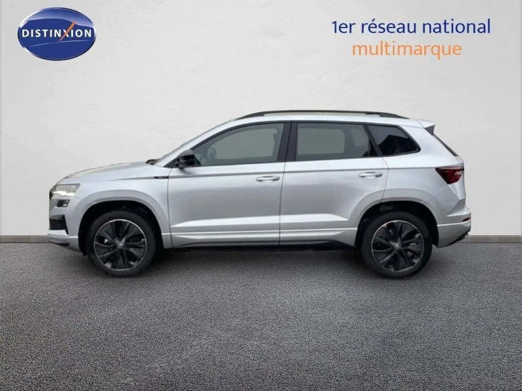 Vue de profil côté gauche d'un Skoda Karoq argent 2025 avec barres de toit et jantes noires sportline.