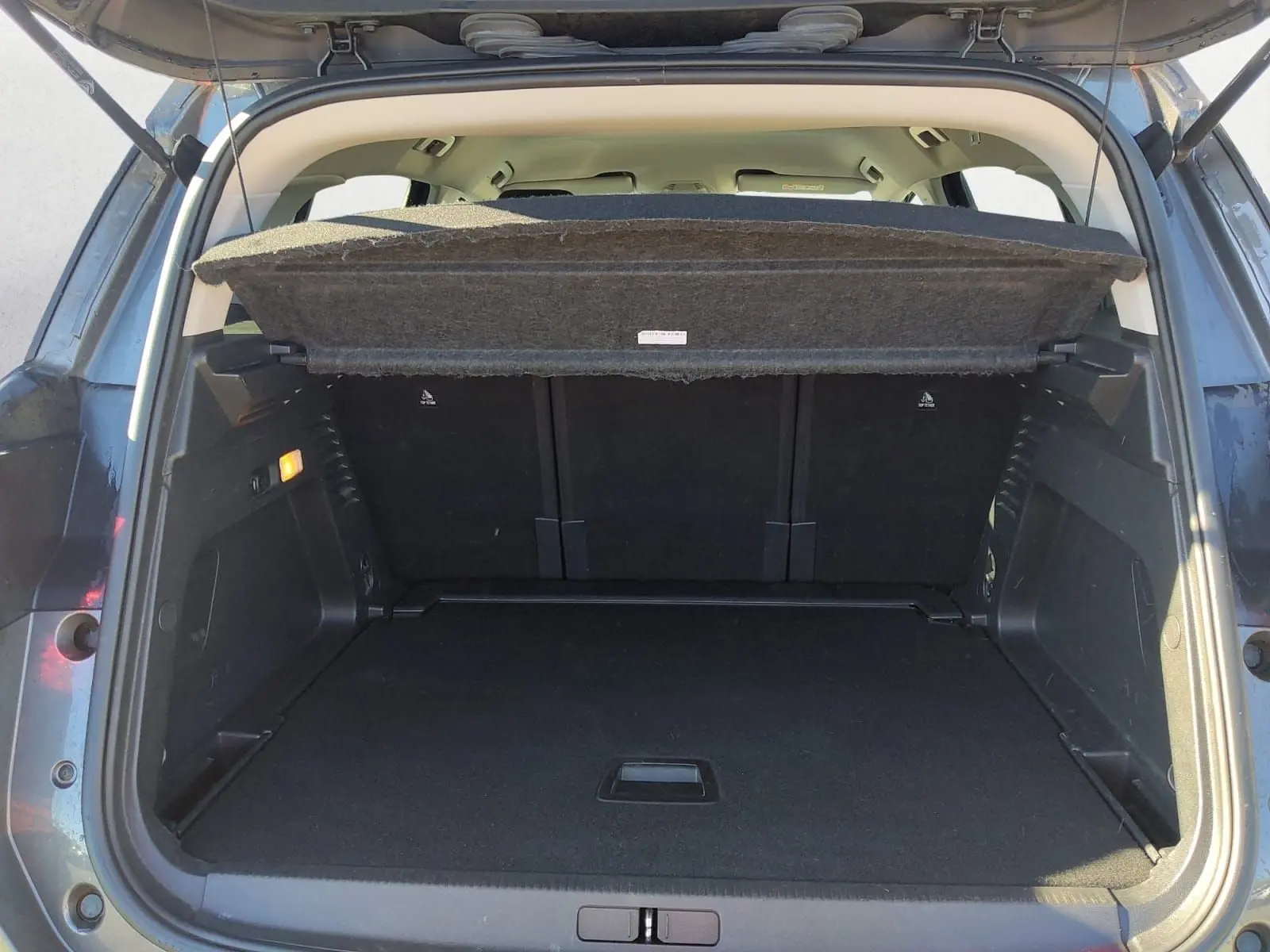 Coffre ouvert vu de l'arrière d'un Citroën C5 Aircross gris platinium, montrant l'espace de chargement vide et la tablette cache-bagages relevée.