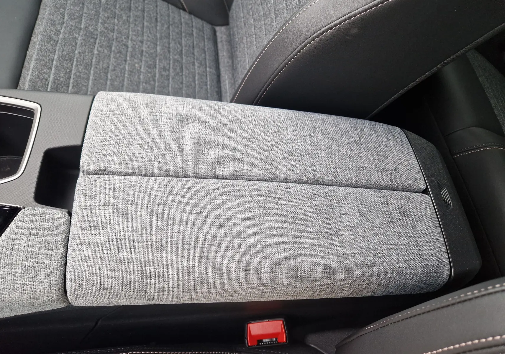 Détail de l'accoudoir central en tissu gris clair du Peugeot 3008 2025, entouré de sièges en cuir noir avec surpiqûres contrastantes.