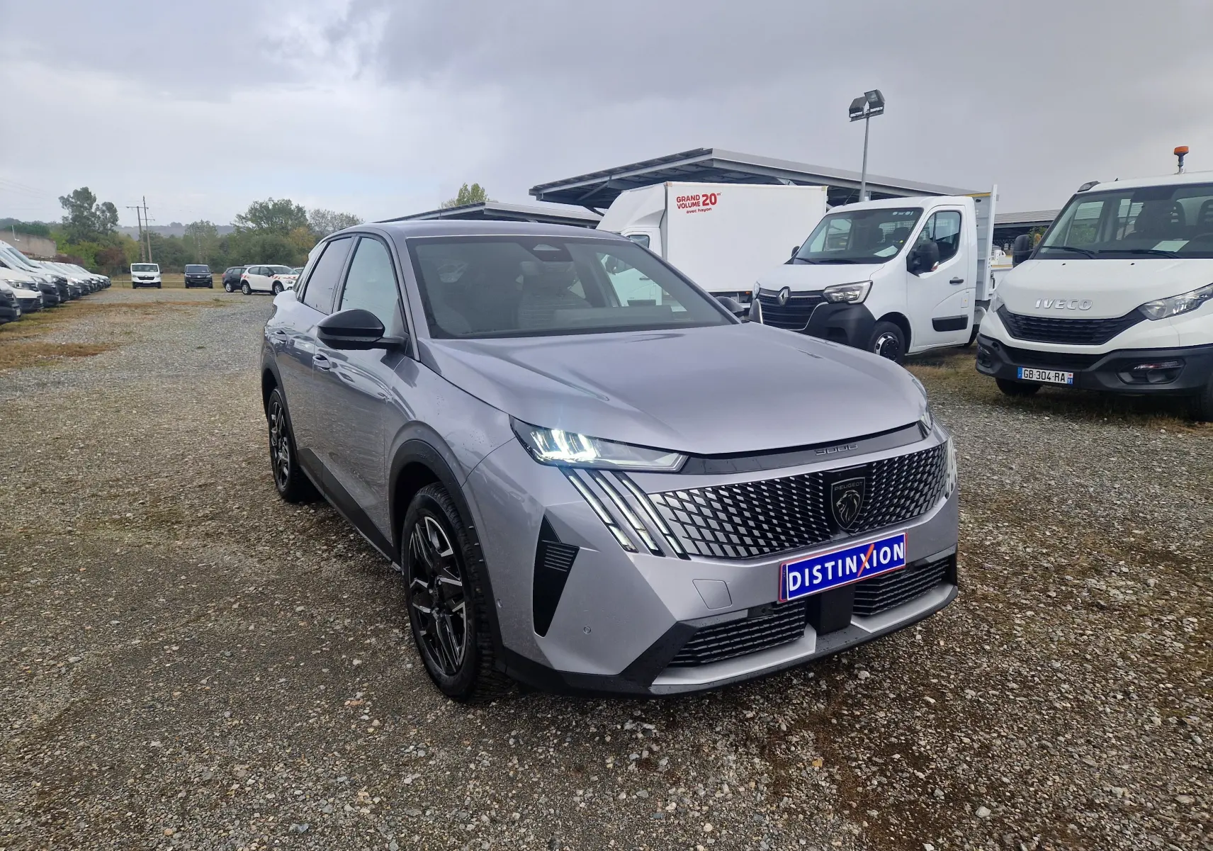 Peugeot 3008 gris Artense vue 3/4 avant droit, calandre distinctive avec logo lion et phares LED allumés.
