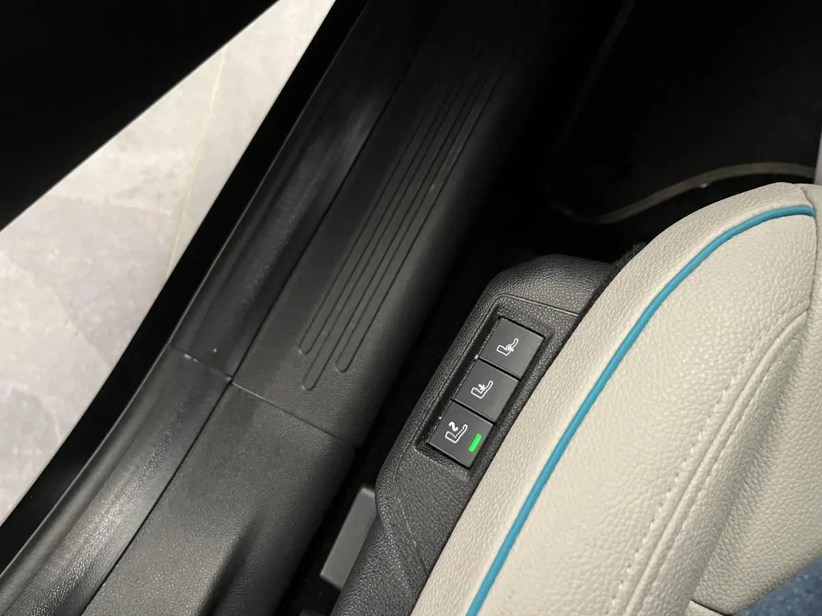 Gros plan sur les commandes de réglage électrique du siège conducteur ivoire soft touch de la FIAT 600 hybride noire.