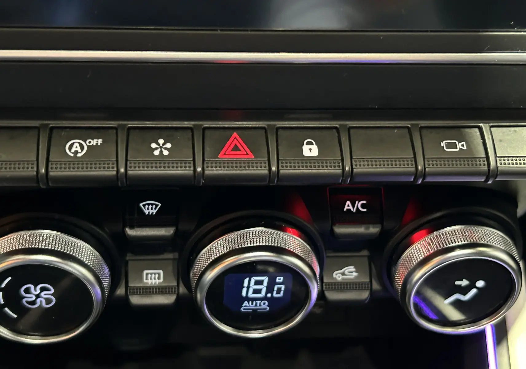 Gros plan sur la console centrale de la Renault Clio V rouge 2023, montrant les commandes de climatisation et les boutons d’alerte et caméra.