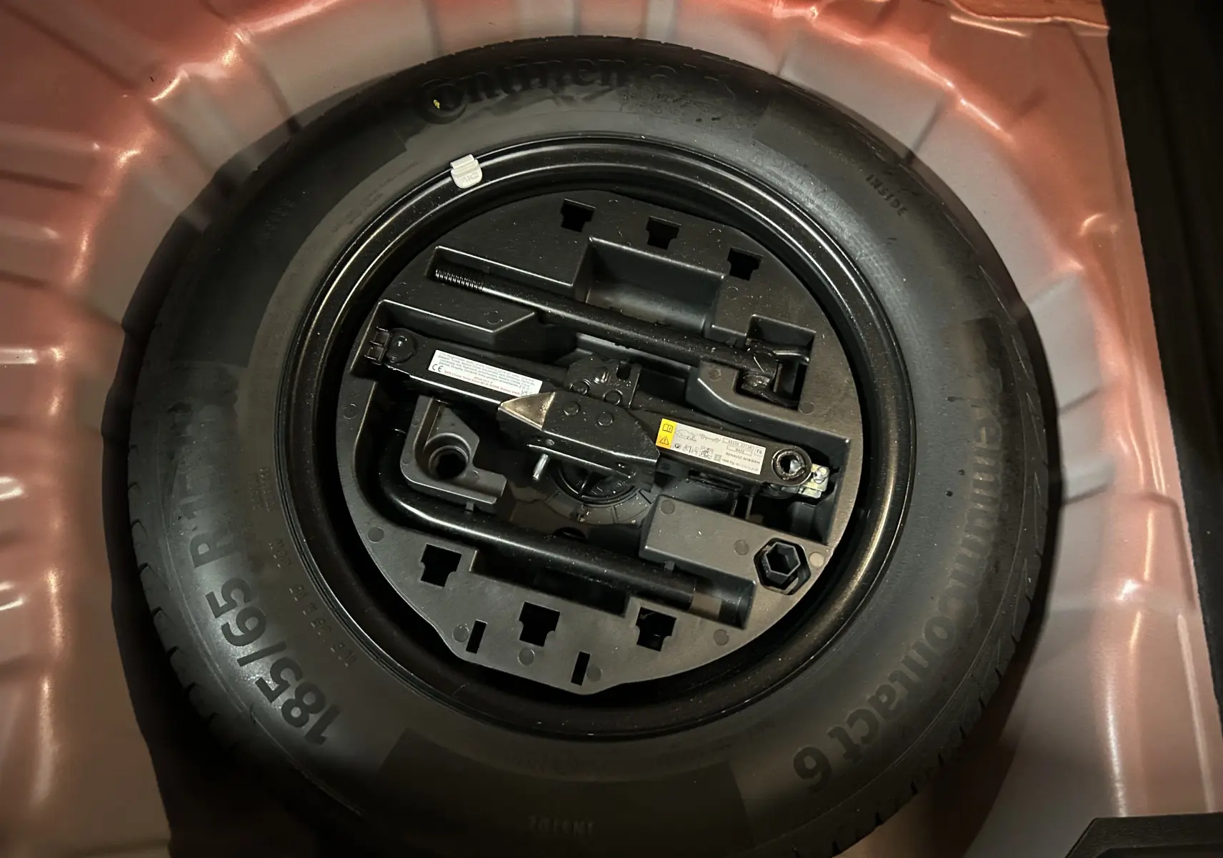 Roue de secours avec outils de changement rangés dans le coffre d'une Renault Clio V rouge 2023.