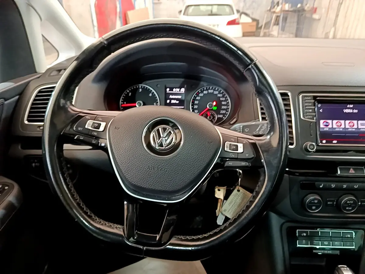 Vue rapprochée du volant cuir noir et du tableau de bord du Volkswagen Sharan 2017, avec écran tactile central allumé.