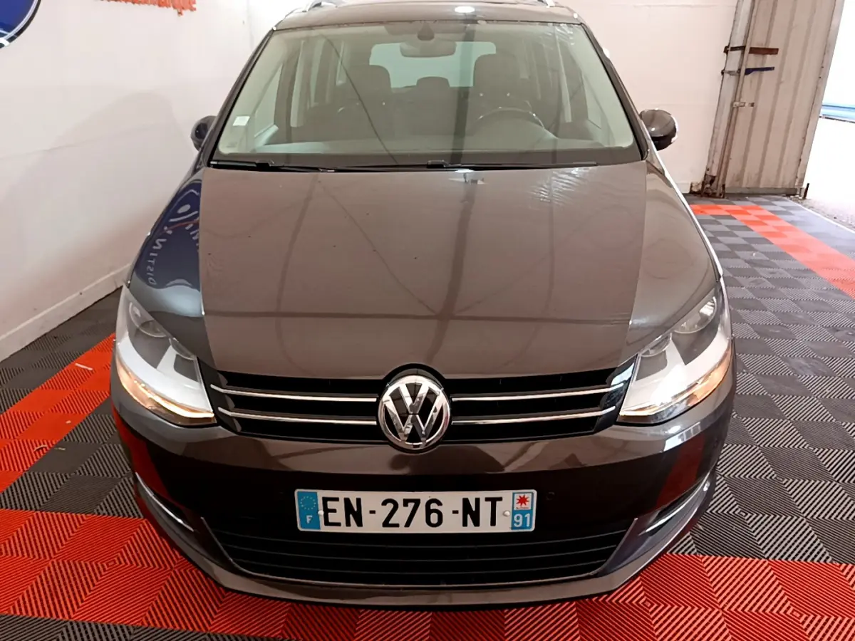 Vue frontale d'un Volkswagen Sharan marron 2017 avec calandre chromée et phares allumés dans un garage.