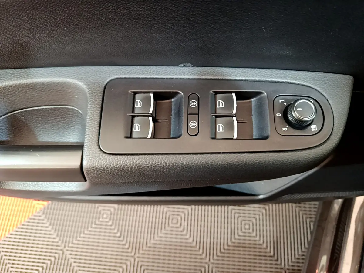 Gros plan sur les commandes de lève-vitres et réglage des rétroviseurs côté conducteur d'un Volkswagen Sharan marron 2017.